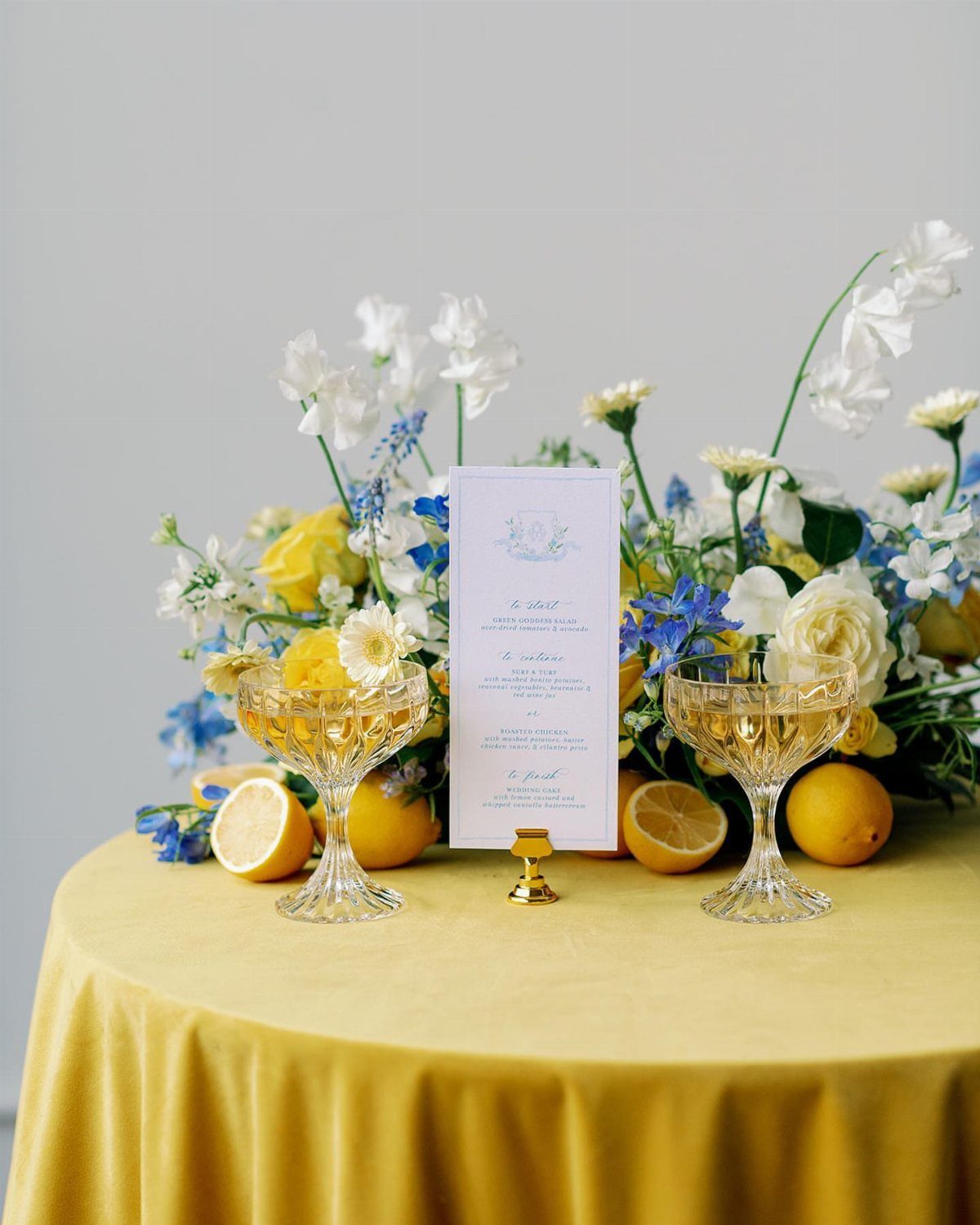 Yellow velvet table setting with blue and white flowers, lemons, and crystal glasses.