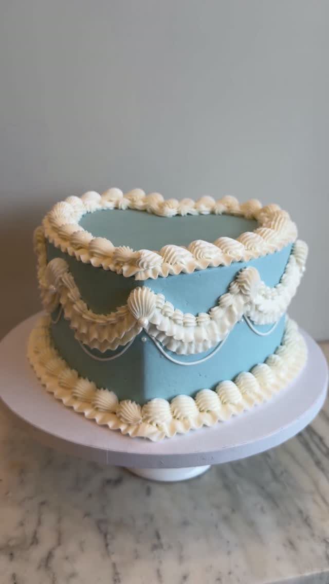 Heart-shaped light blue cake with white decorative frosting on a white stand.