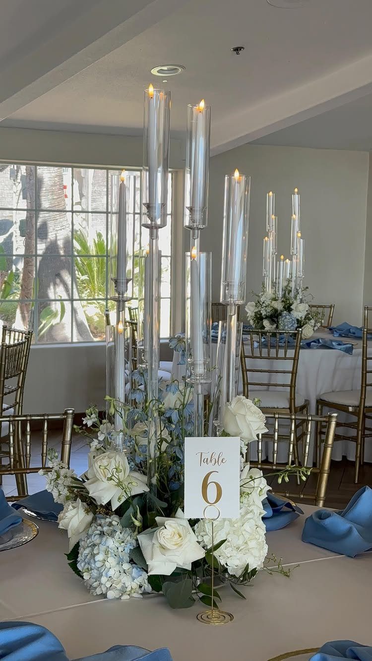 Wedding table centerpiece with tall candles, white roses, and dusty blue hydrangeas.
