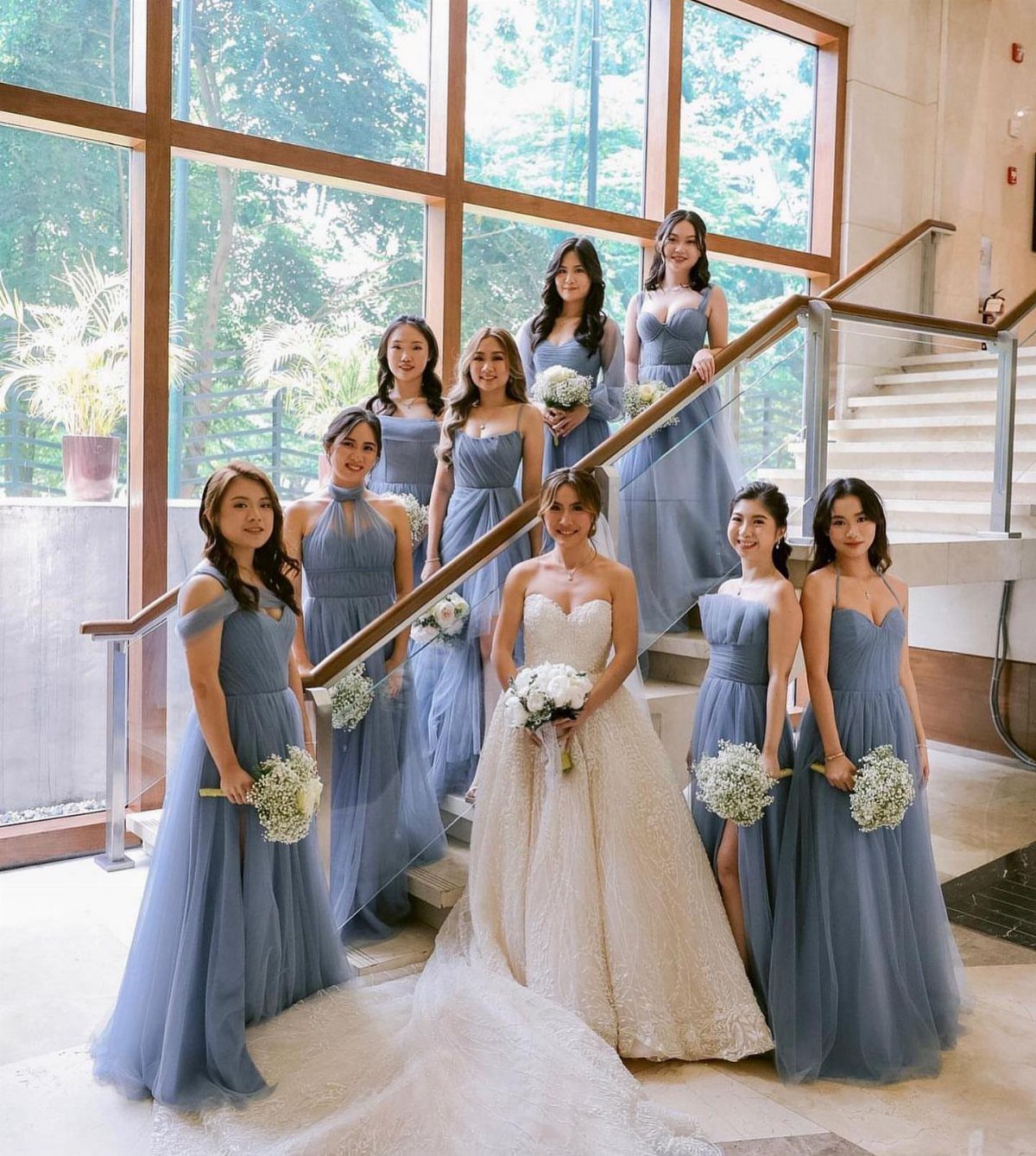 Bride in white gown surrounded by bridesmaids in light blue dresses on stairs