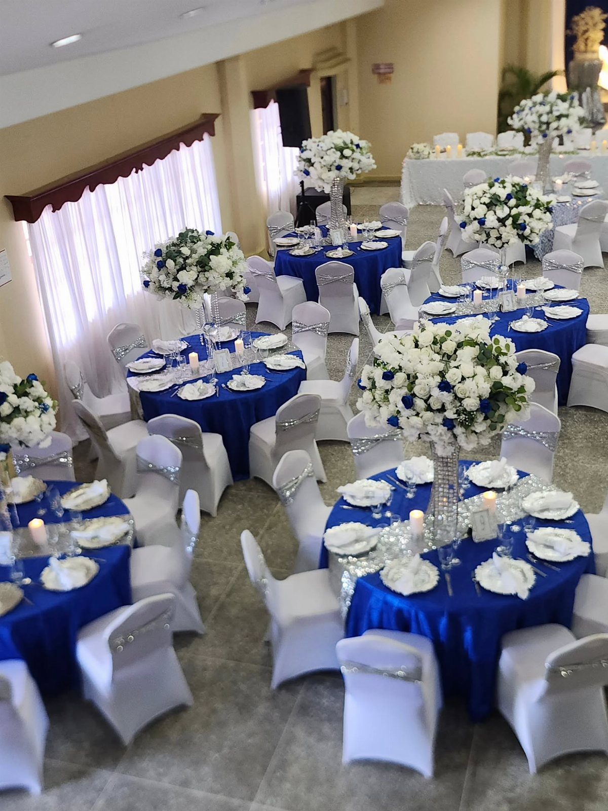 Sapphire blue tablecloths on round wedding tables with white floral centerpieces and chairs.