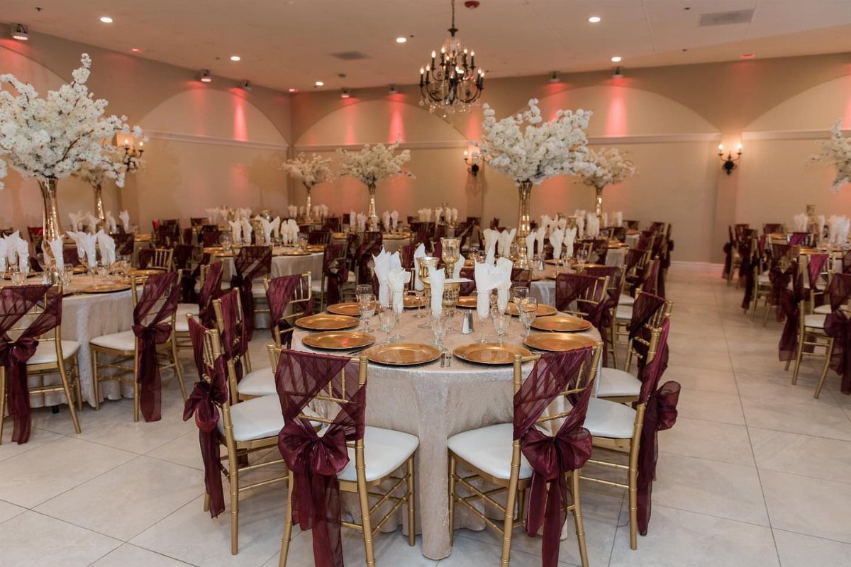 Champagne table linens and gold chairs with maroon sashes in a banquet hall.