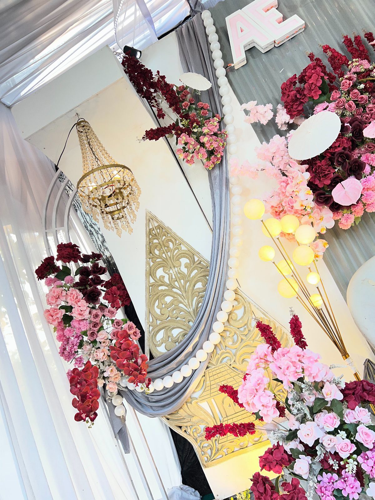 Maroon and pink flowers decorating a gold panel with grey fabric draping.