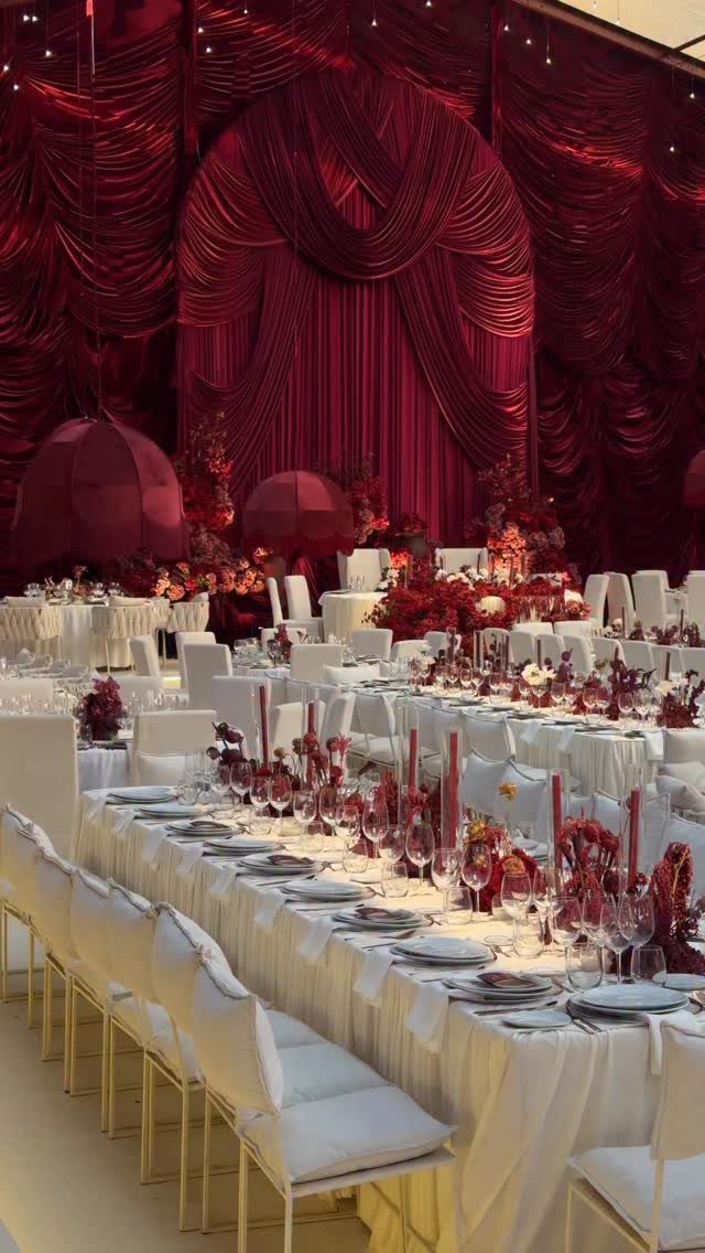 Long white banquet table with burgundy floral centerpieces and red draped curtains background