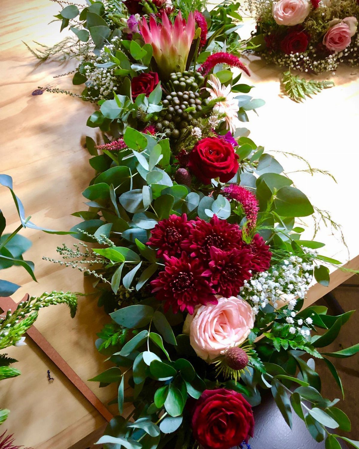 Burgundy and sage floral arrangement with deep red roses and green eucalyptus leaves.