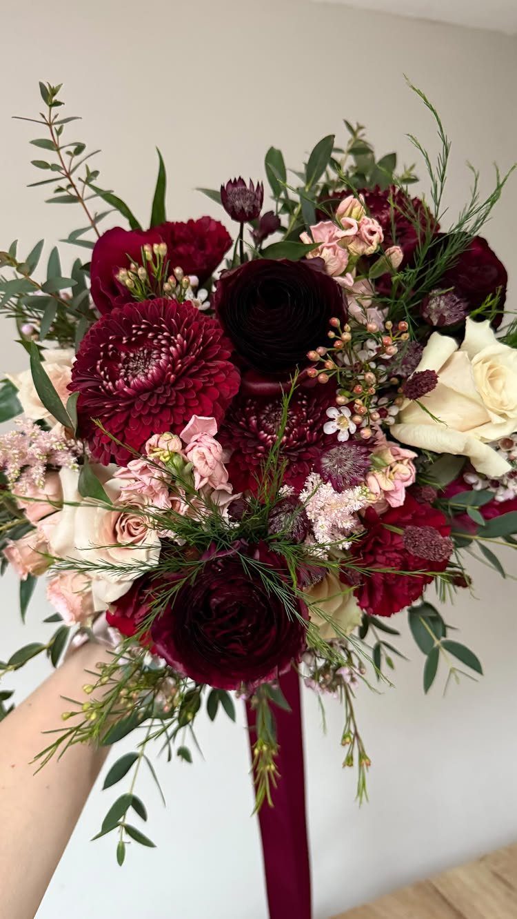 Bridal bouquet with deep maroon dahlias, white roses, and green eucalyptus leaves.