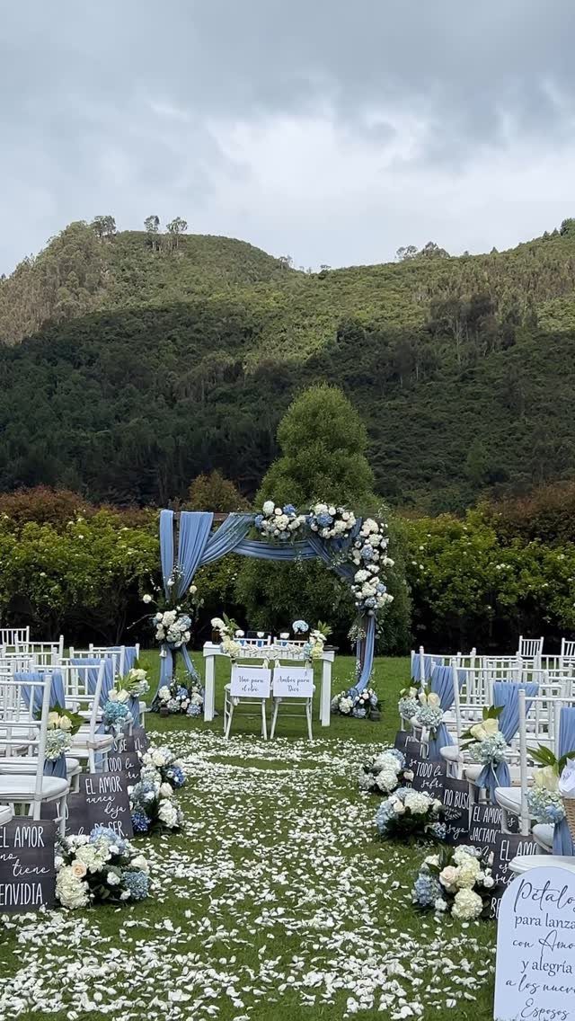 Outdoor wedding ceremony setup with dusty blue fabric arch and white floral arrangements.