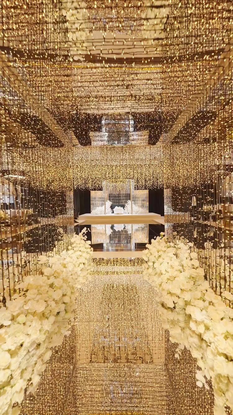 Gold beaded curtains and white floral arrangements in a shimmering, reflective wedding venue.