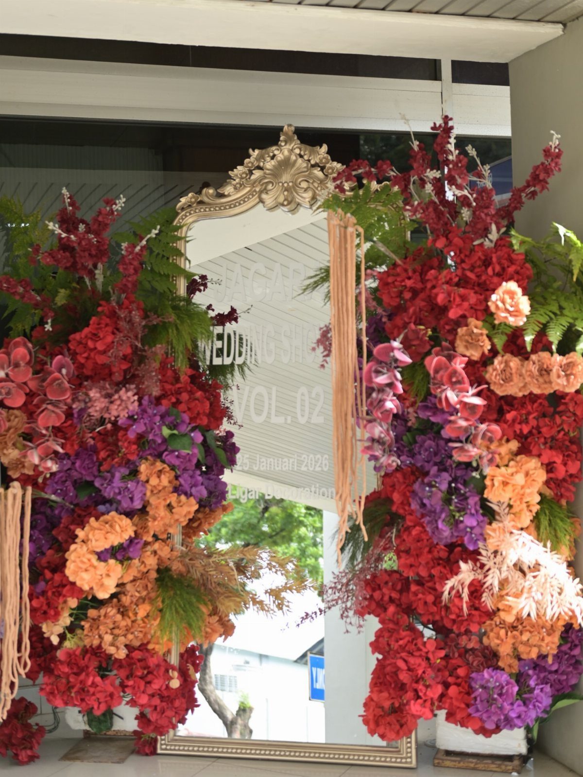 Ornate gold mirror surrounded by vibrant red, orange, and purple floral arrangements.