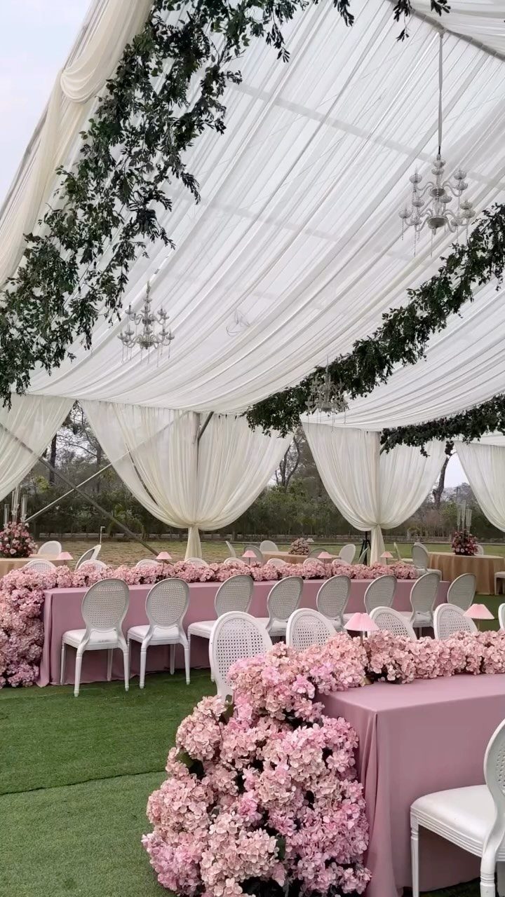 Soft blush pink table linens and floral garlands under a white draped canopy.