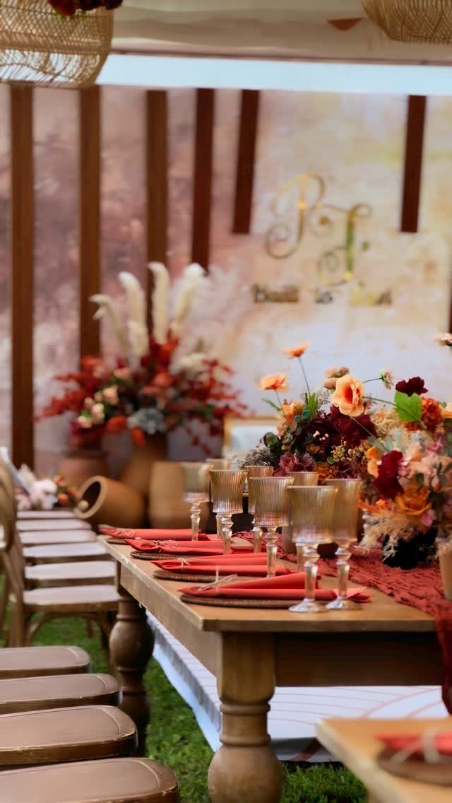 Wooden wedding table with terracotta napkins and autumn floral centerpieces in an outdoor setting.