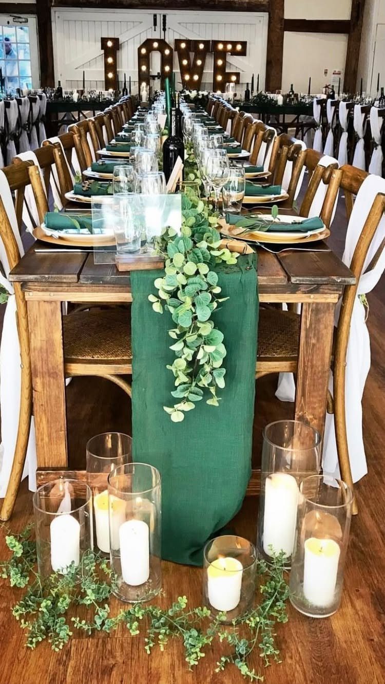 Wooden wedding table with emerald green runners, greenery, and white pillar candles.