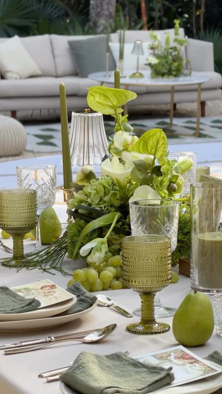 Green wedding table setting with floral centerpieces, green glassware, and sage napkins.