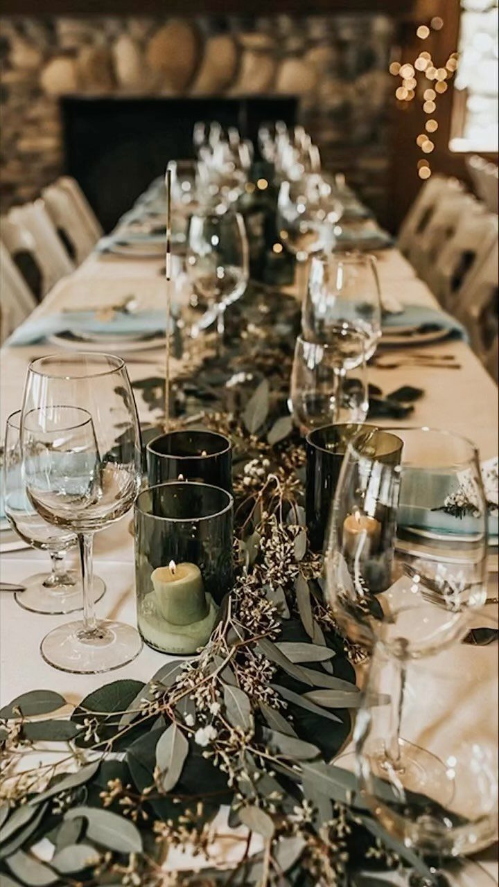 Wedding table setting with green foliage runner, grey candle holders, and clear glassware.