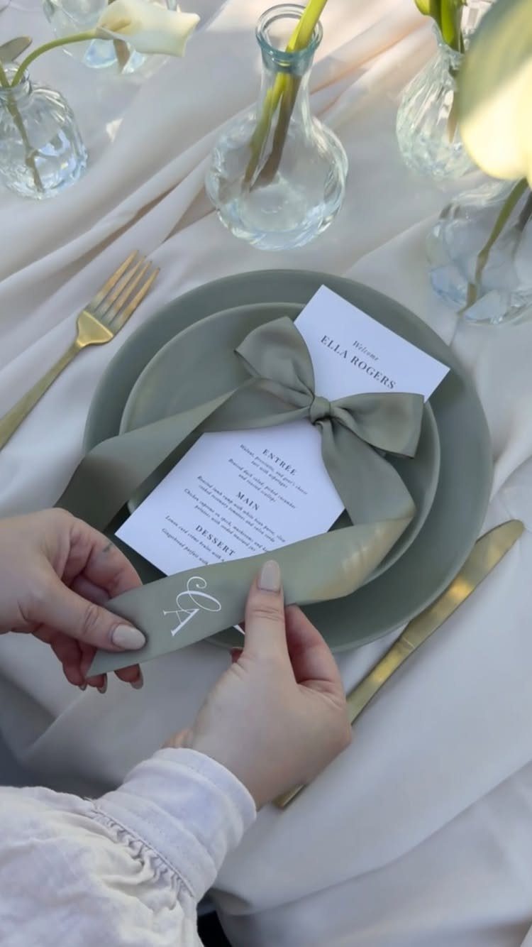 Sage green plate and ribbon on ivory tablecloth with gold cutlery and flowers