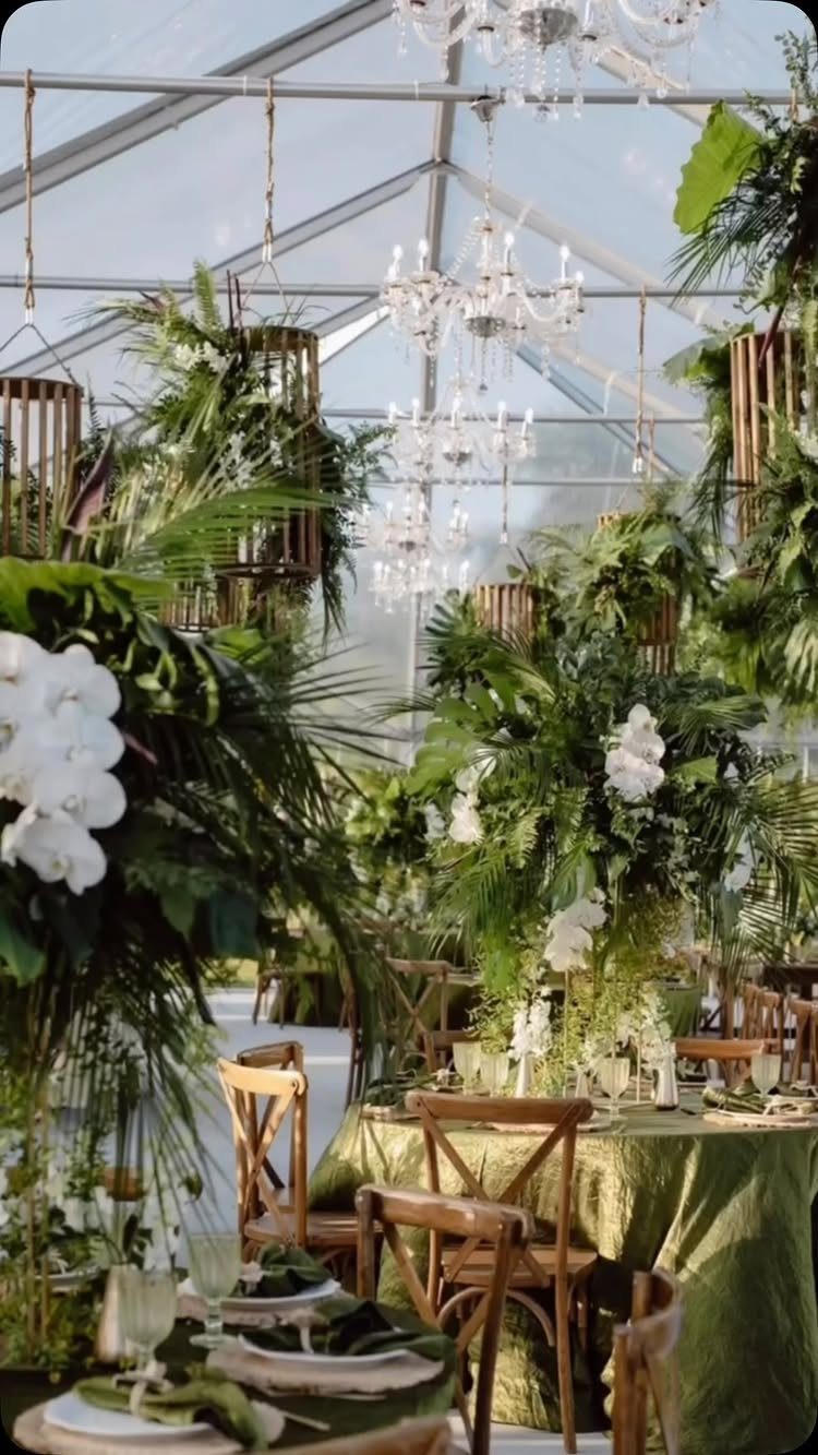 Tropical greenery and white orchids decorating a wedding reception under a clear tent.