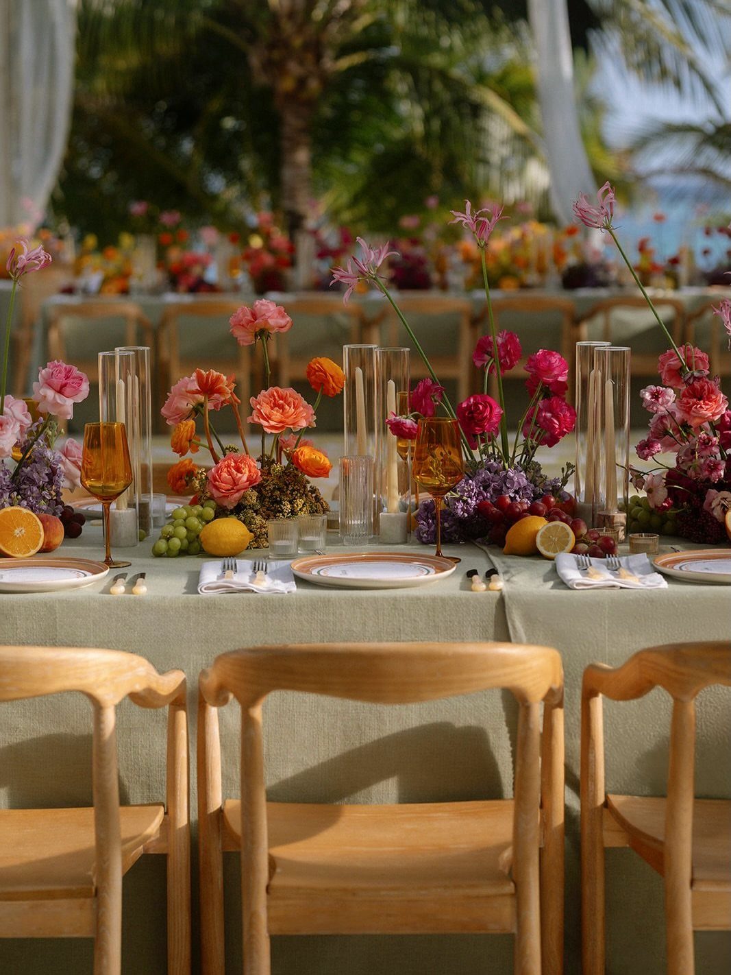 Elegant table setting with colorful flowers, citrus fruits, and amber glasses outdoors.