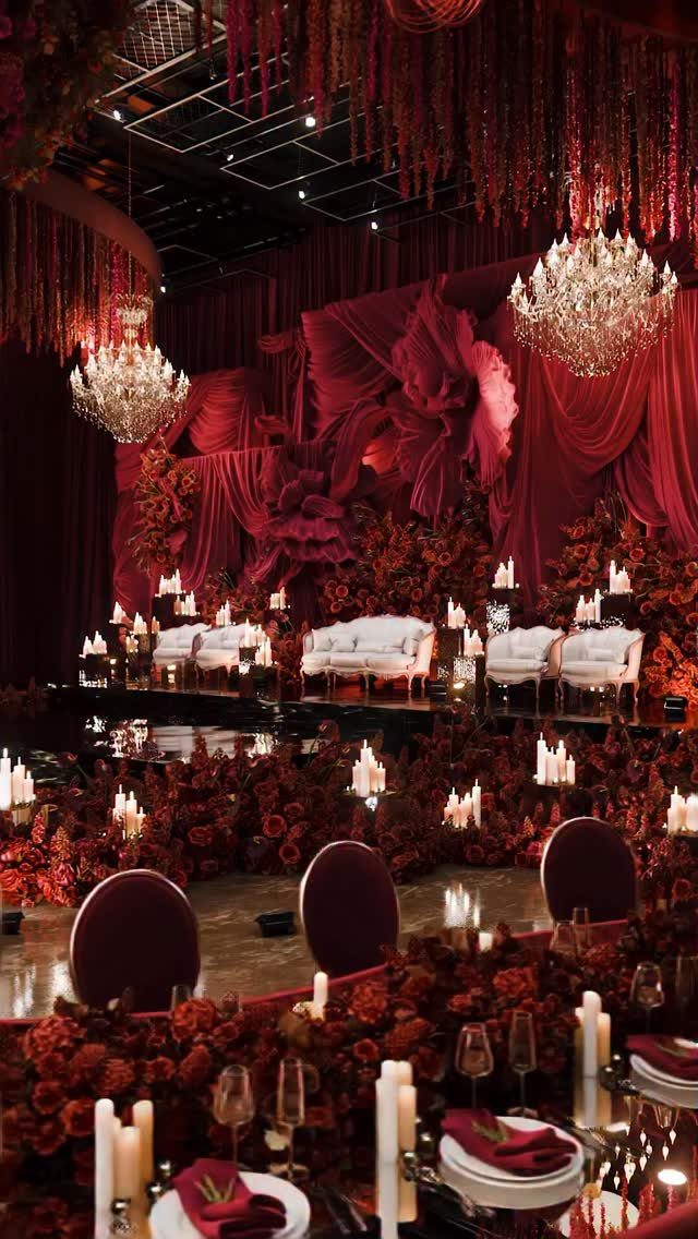 Opulent wedding reception with red floral arrangements, crystal chandeliers, and elegant table settings.