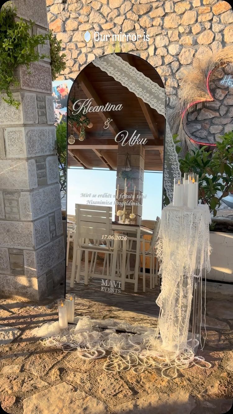 Arched mirror reflecting wedding tables next to a lace-covered candle pedestal and stone wall
