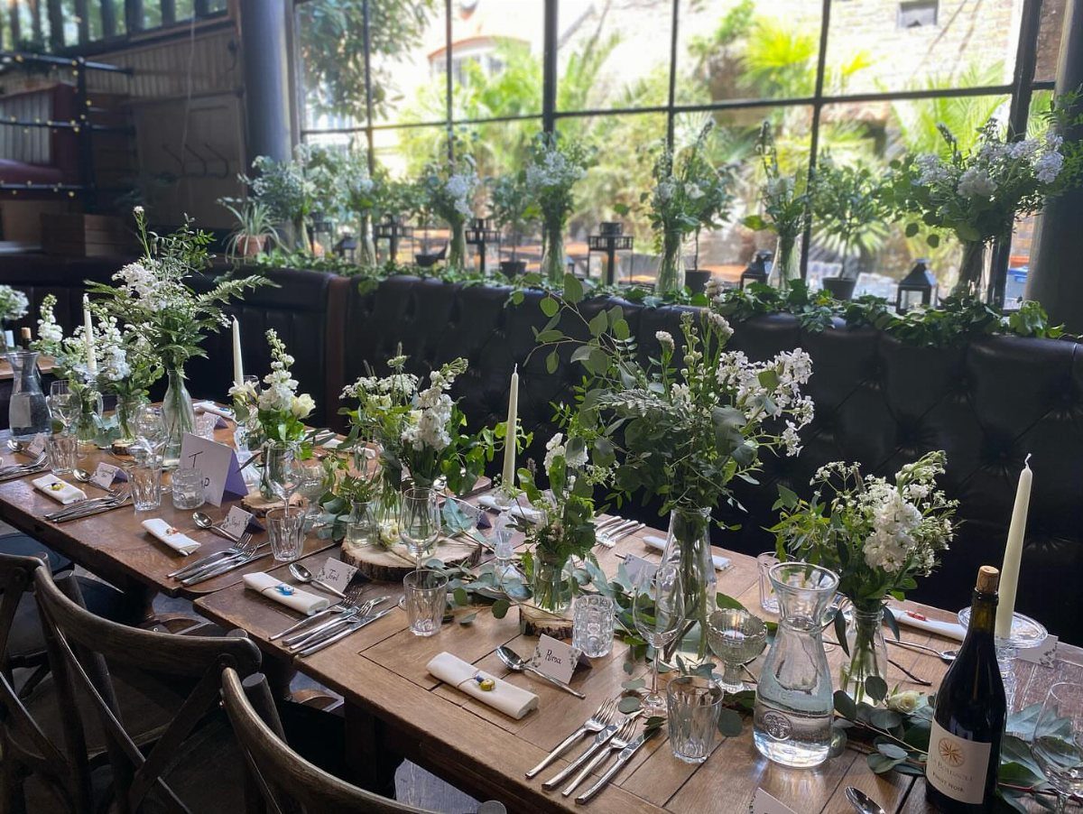 Wooden dining table decorated with white flowers, greenery, and white taper candles.