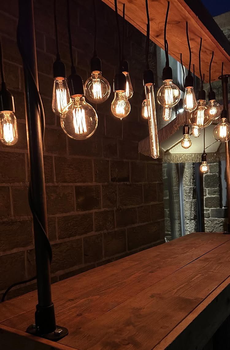 Glowing Edison bulbs hanging from black cords over a rustic wooden bar counter.