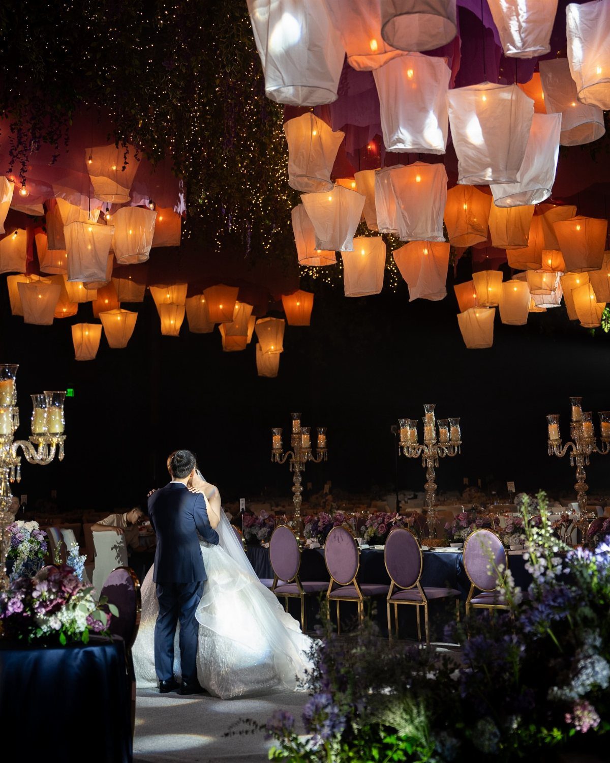 Glowing white and orange hanging lanterns above a bride and groom at a wedding