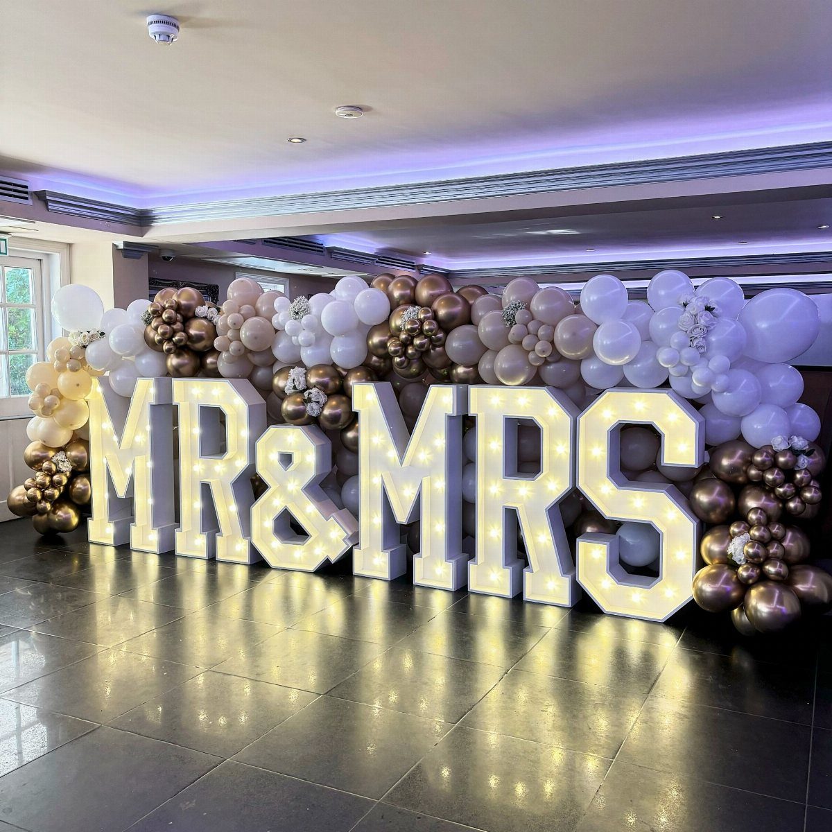 Large illuminated MR & MRS letters with a white and gold balloon backdrop.