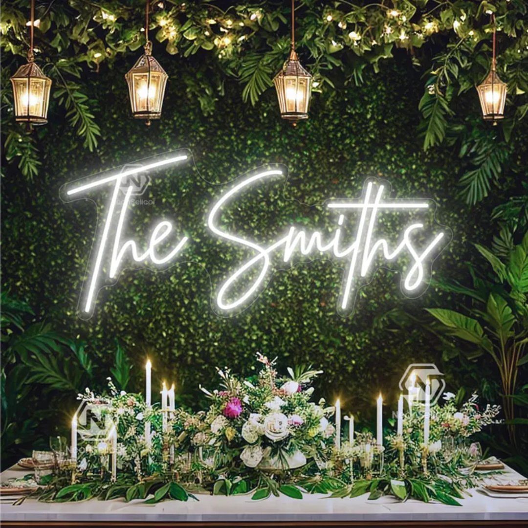White neon sign reading The Smiths on a green hedge wall with lanterns.