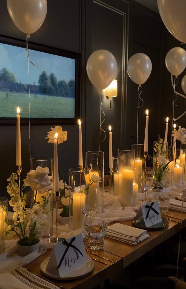 Elegant table setting with white balloons, floral arrangements, and various white candles.