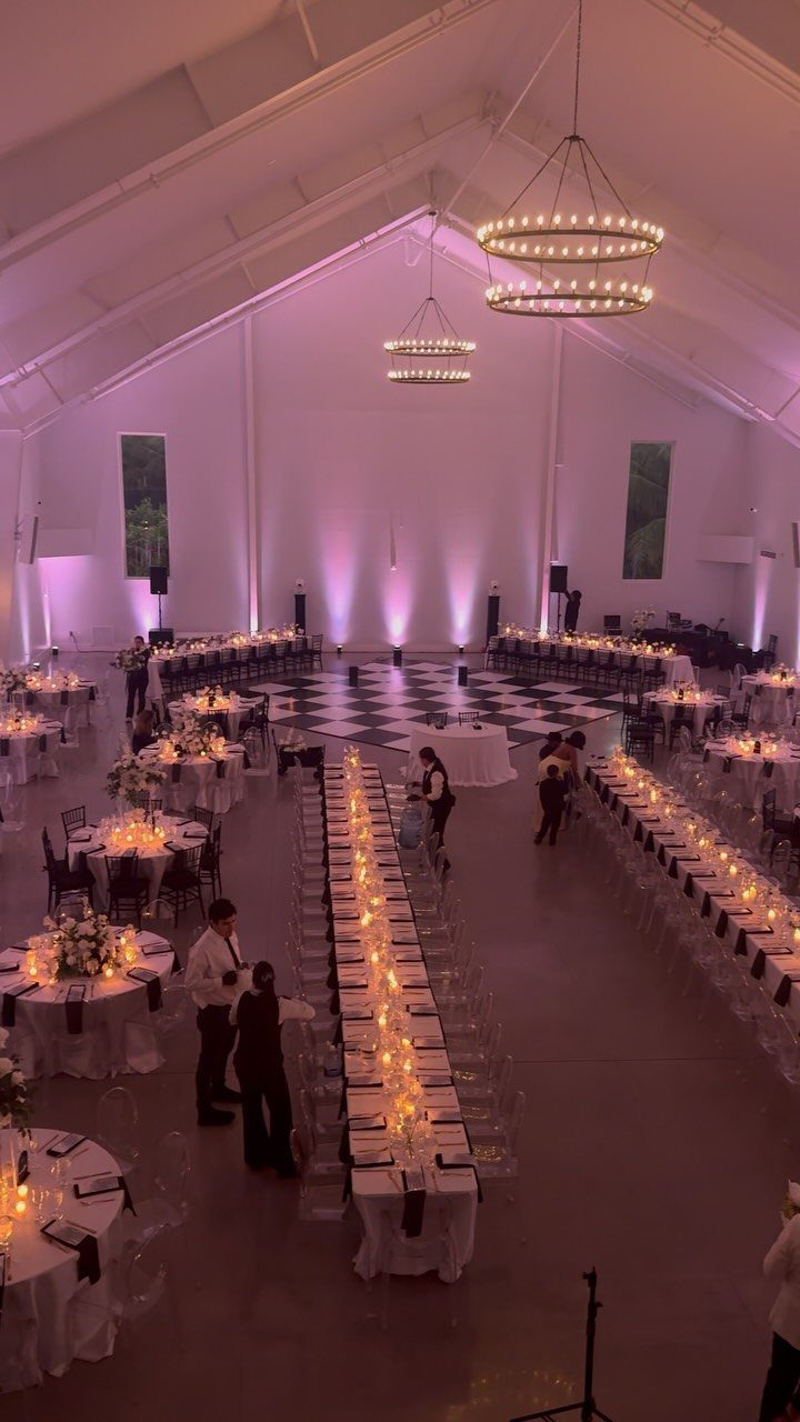 Wedding reception hall with purple uplighting on walls and large circular chandeliers above.