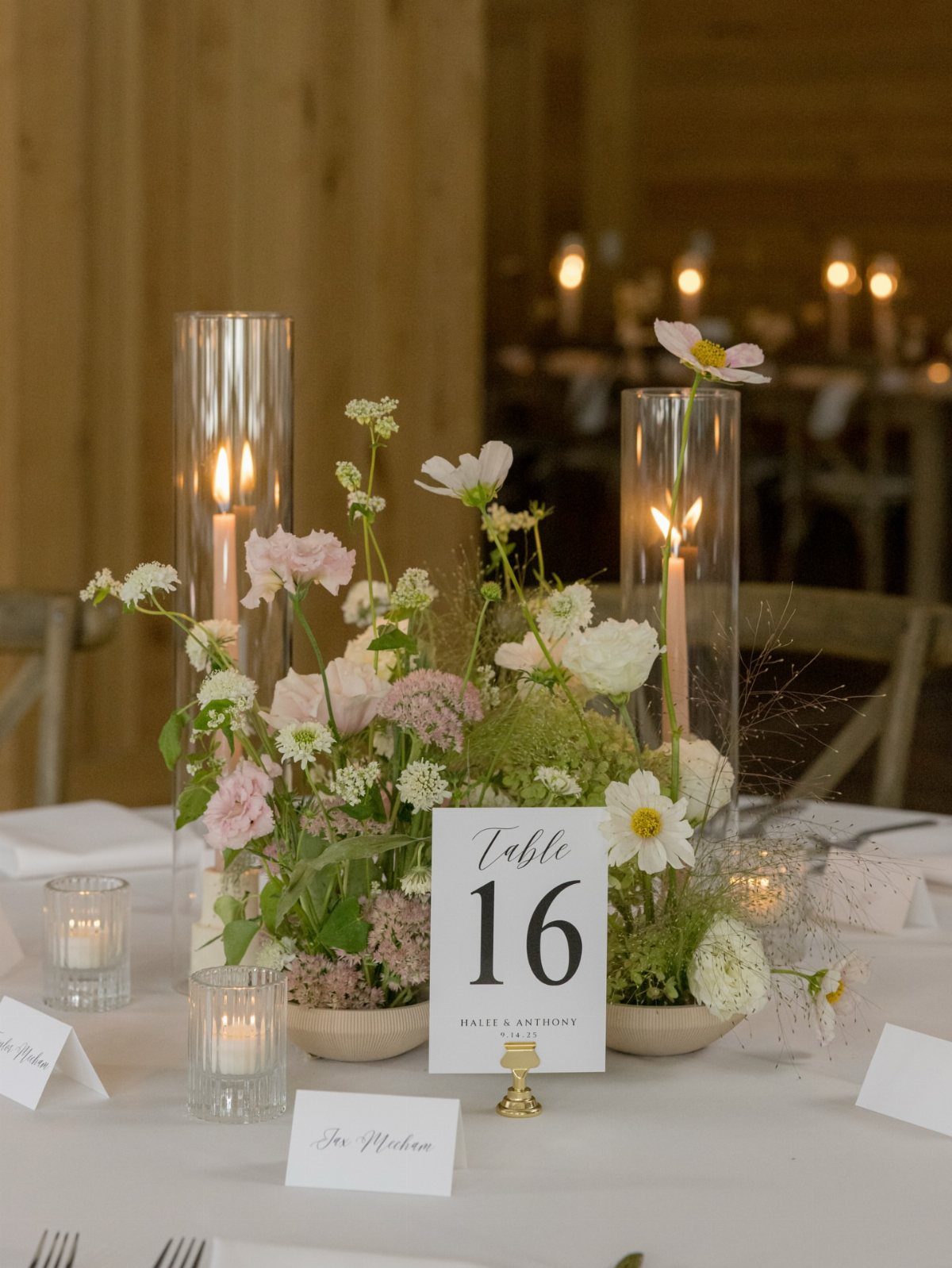 Floral centerpiece with tall cylinder candles and table number 16 on white tablecloth