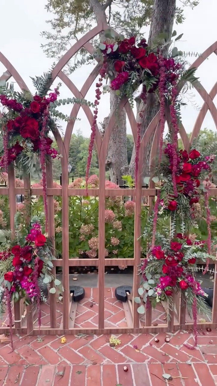Wooden garden arbor decorated with red roses and greenery on a brick patio