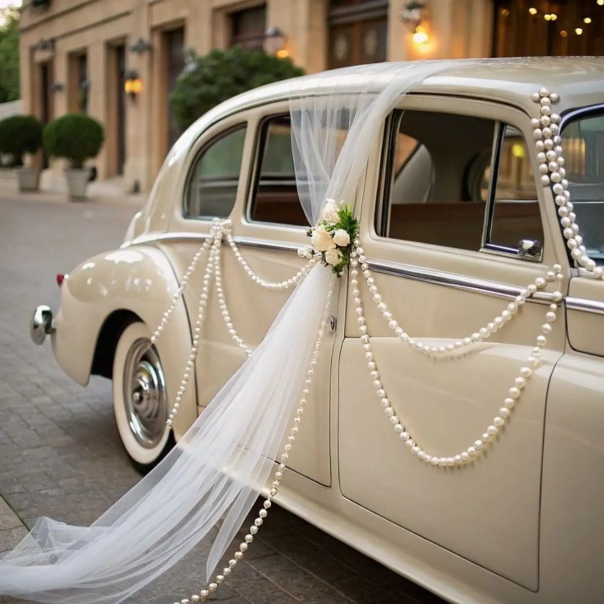 Cream vintage wedding car decorated with white tulle, pearls, and white roses.