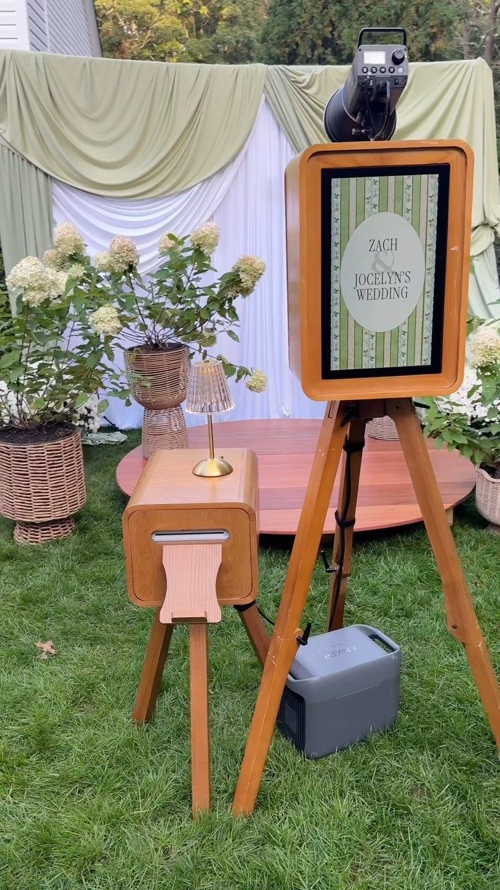 Wooden vintage photo booth and print station set up outdoors with draped backdrop.