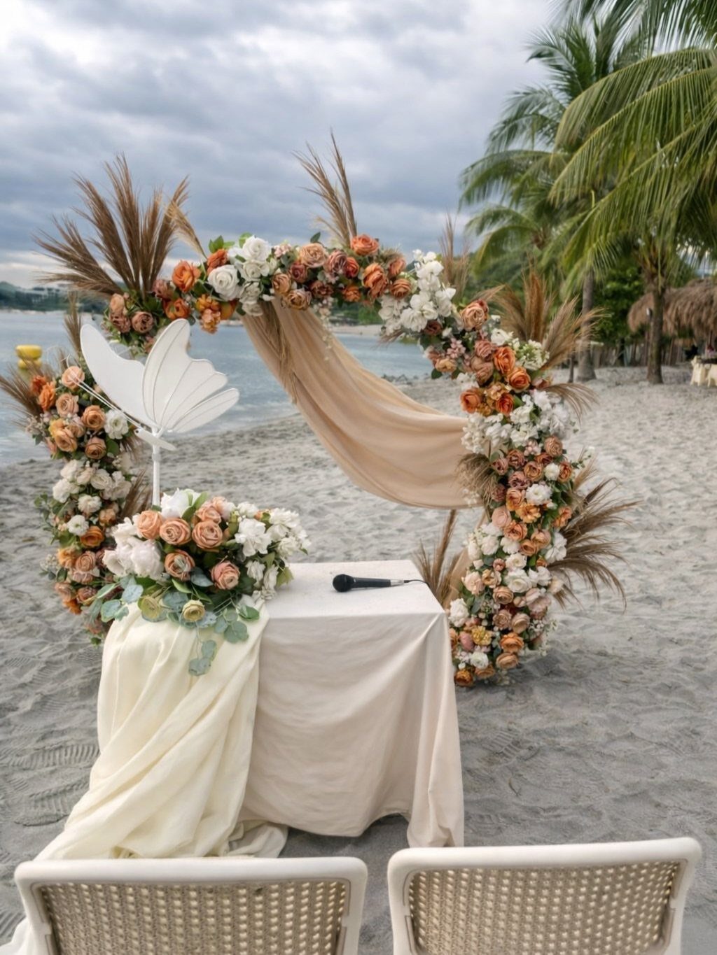 Circular floral wedding arch with orange roses and beige fabric on a sandy beach