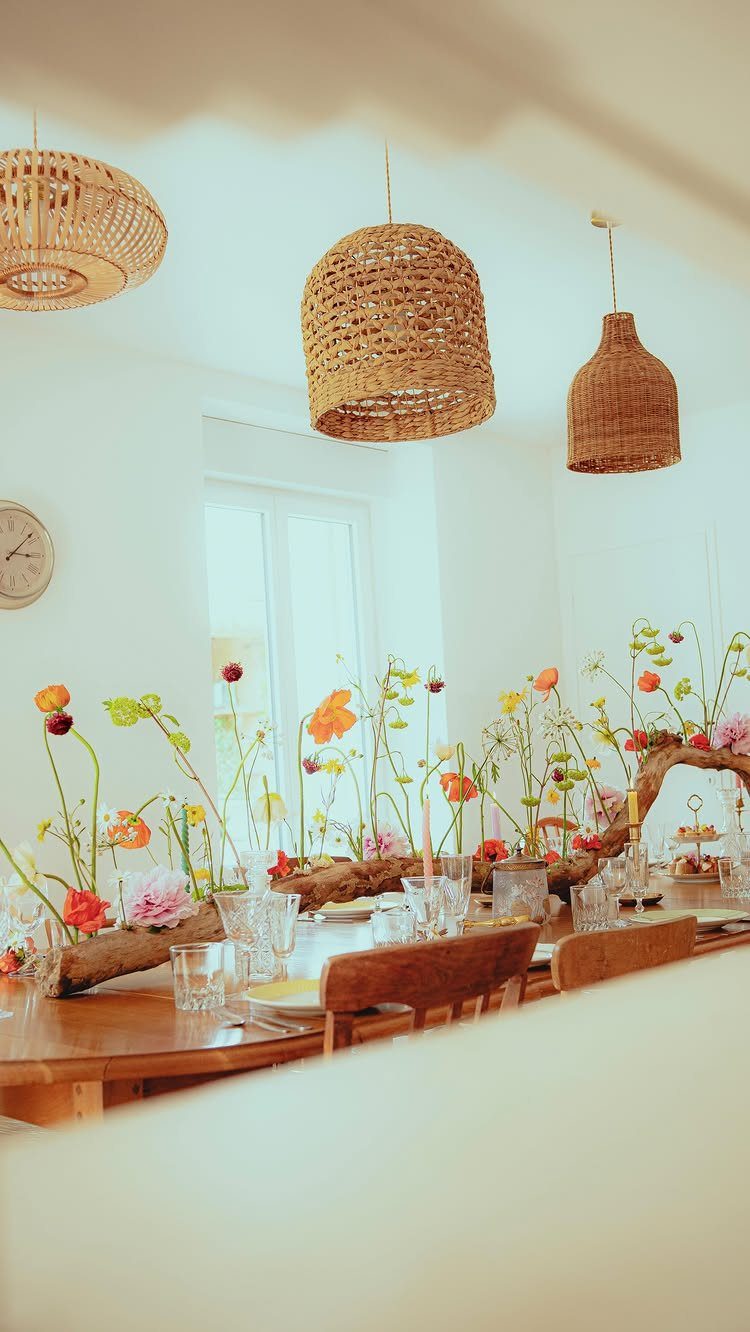 Wooden dining table with driftwood and wildflower centerpiece under woven rattan pendant lights