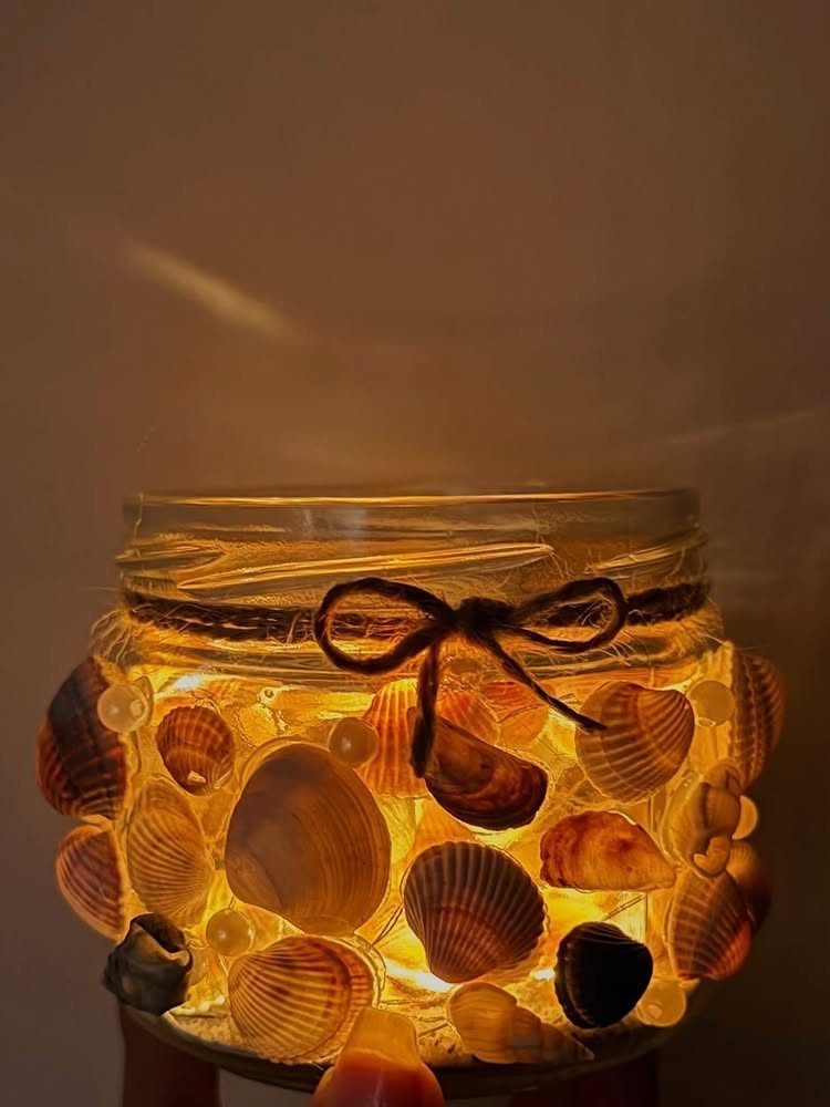 Shell decorated glass jar with warm internal lighting and a twine bow.