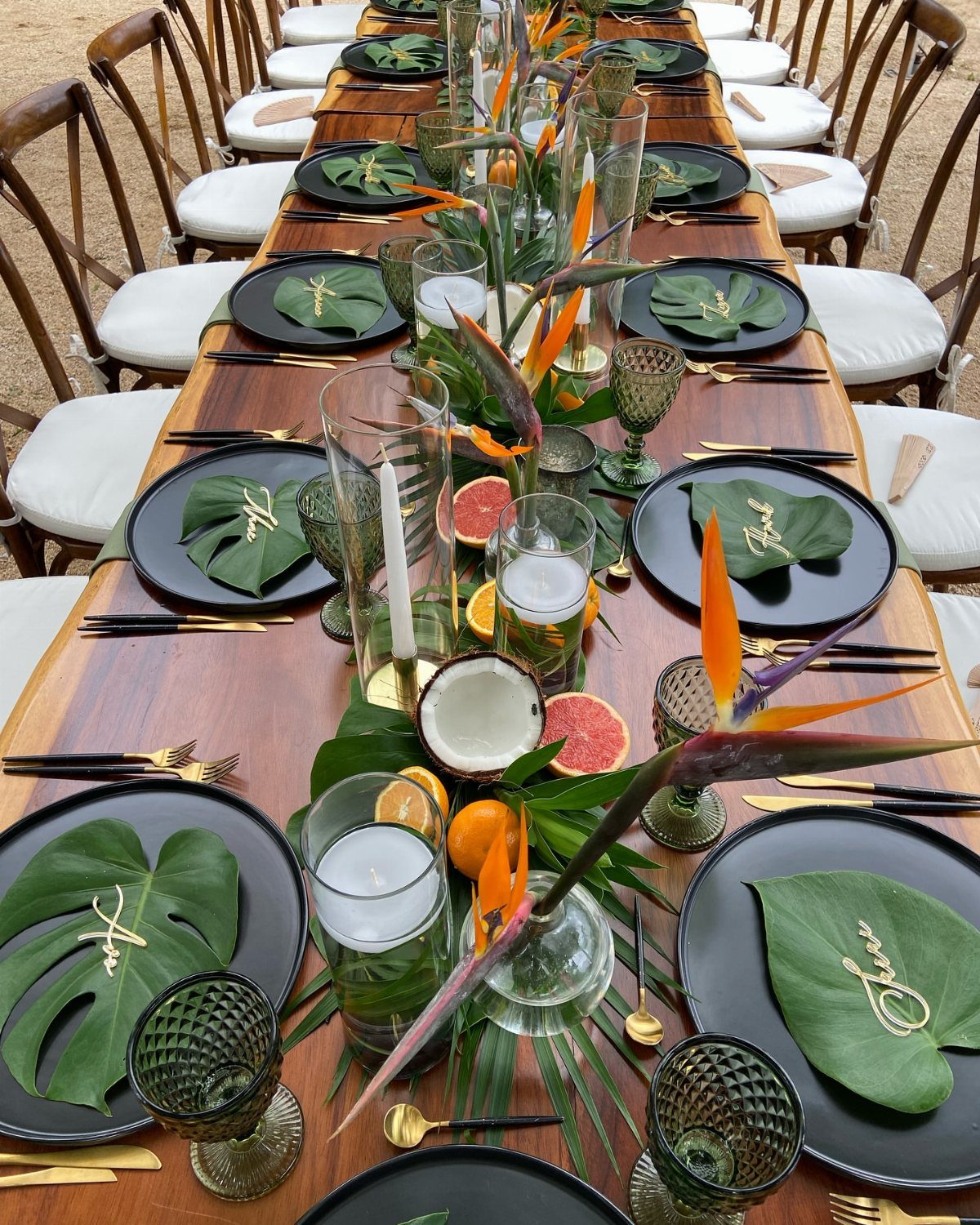 Tropical wedding table setting with black plates, green leaves, and bird-of-paradise flowers.