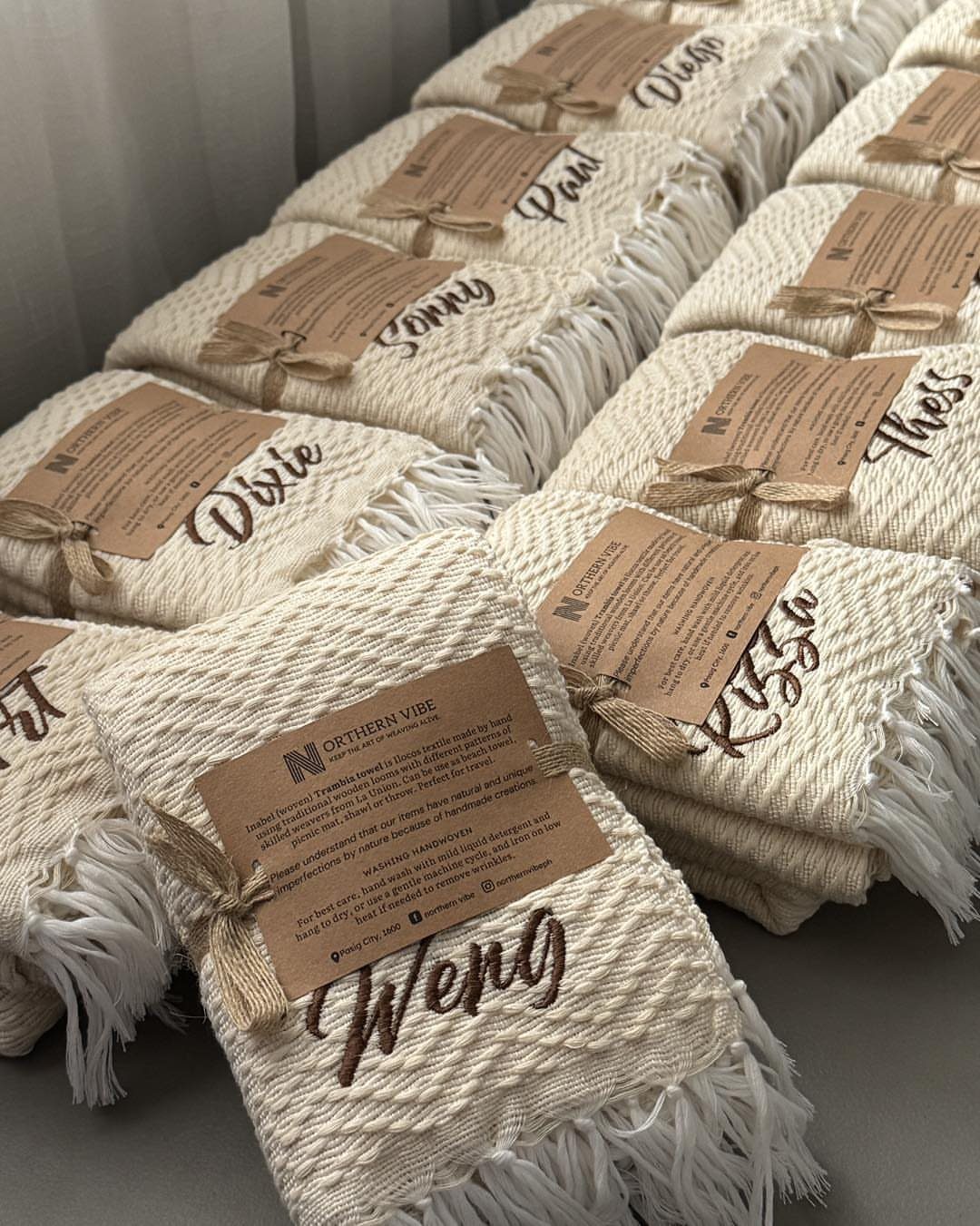 Folded cream beach towels with embroidered names and kraft paper gift tags.
