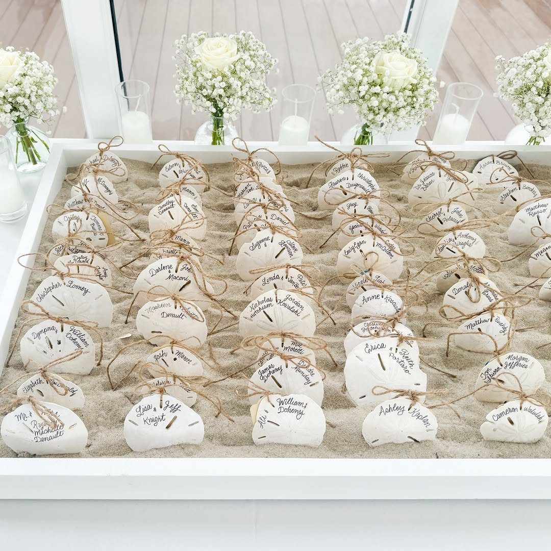 White stones with handwritten names tied with twine resting on sand in a tray