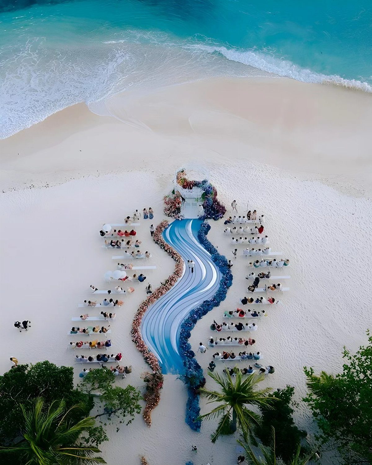 Winding blue wave-shaped wedding aisle on a white sand beach with guests.