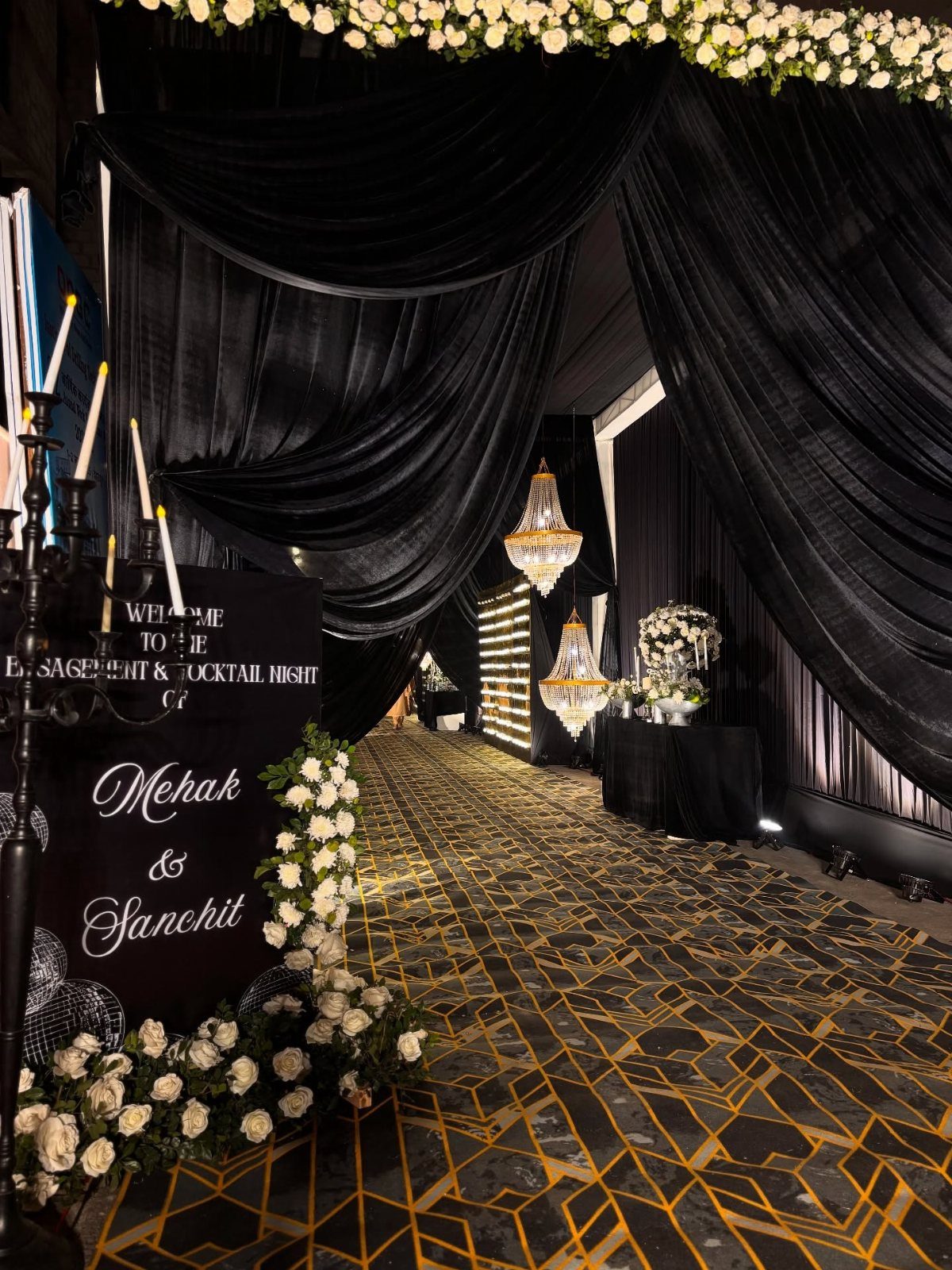 Black candelabra with white candles beside a welcome sign and black fabric drapes.