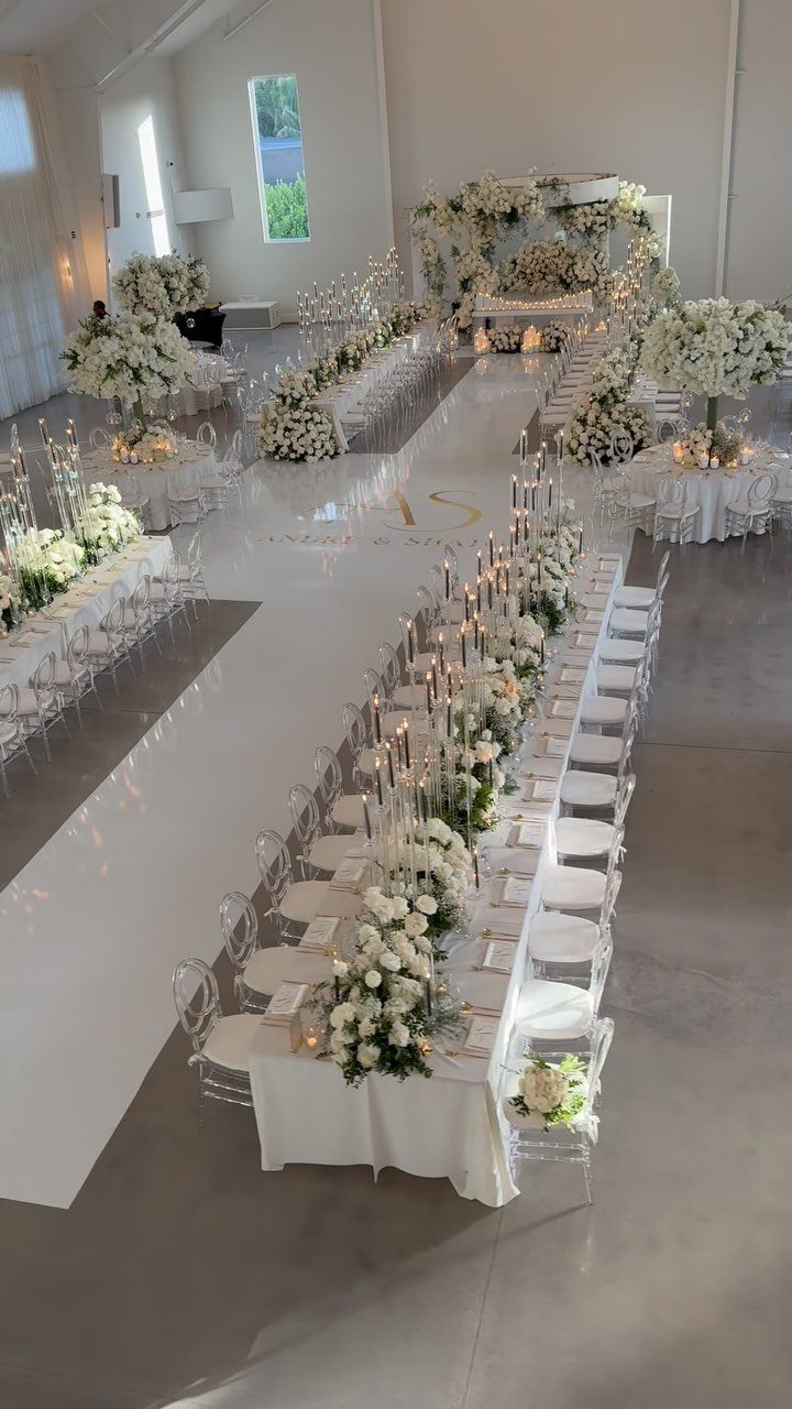 Long wedding table with a low arrangement of white flowers and lit candles.