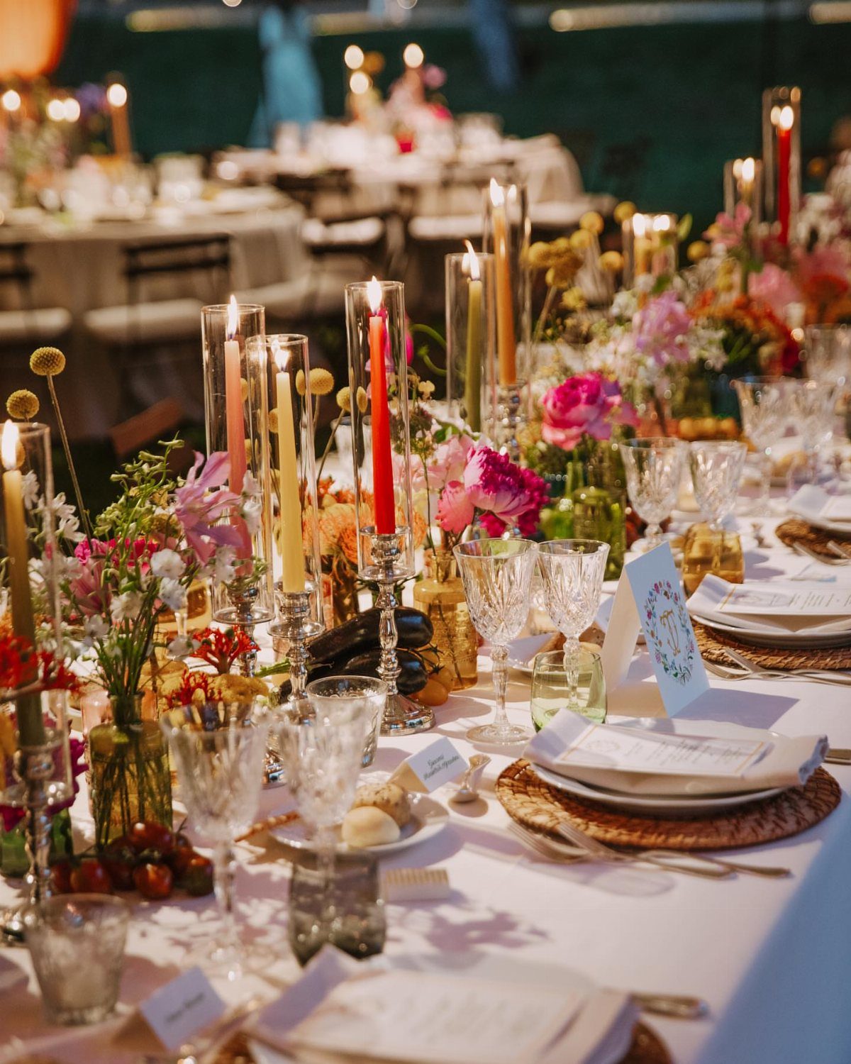 Colorful taper candles in crystal holders and floral centerpieces on a wedding table.