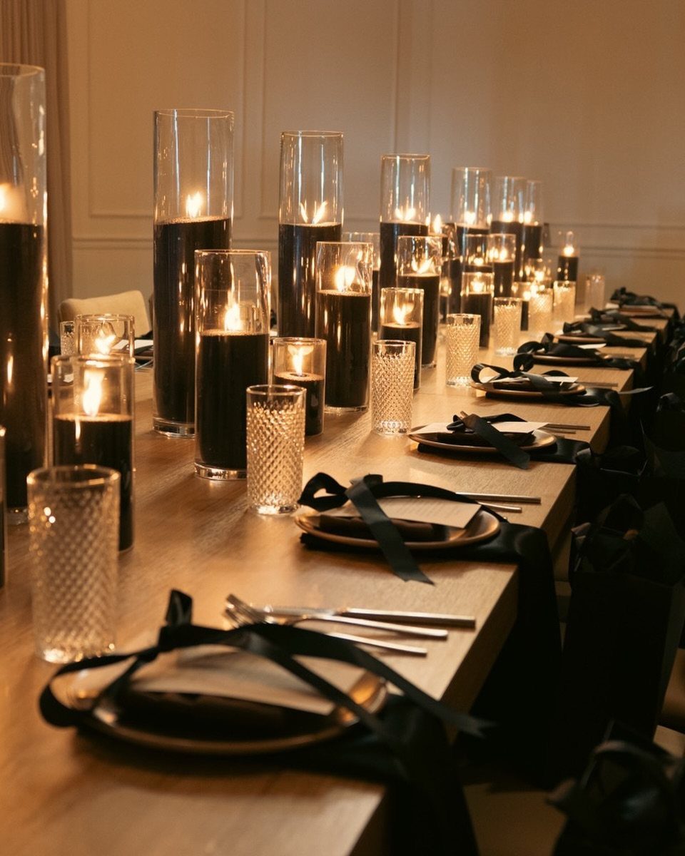 Black floating candles in clear glass cylinders on a wooden wedding table.