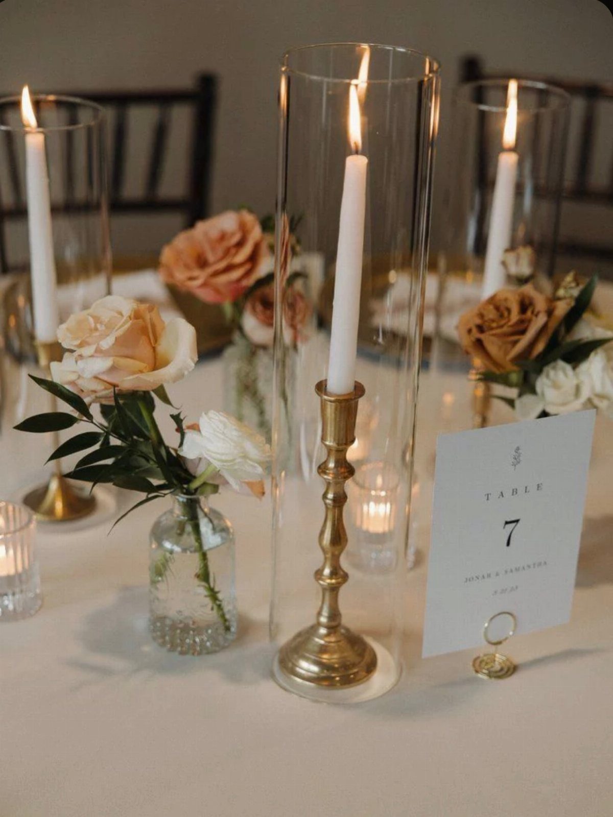 White taper candles in brass holders and glass cylinders with peach roses.