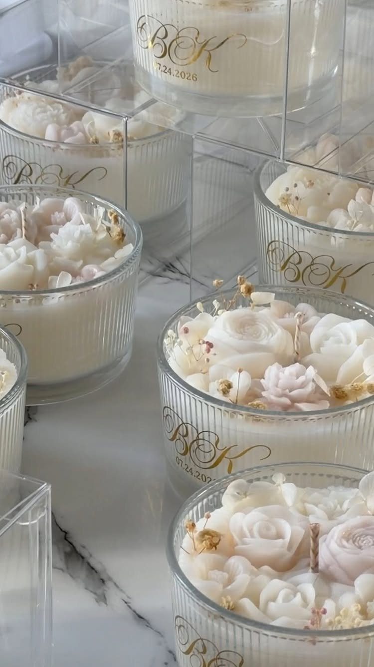 White candles in ribbed glass jars with wax roses on a marble surface