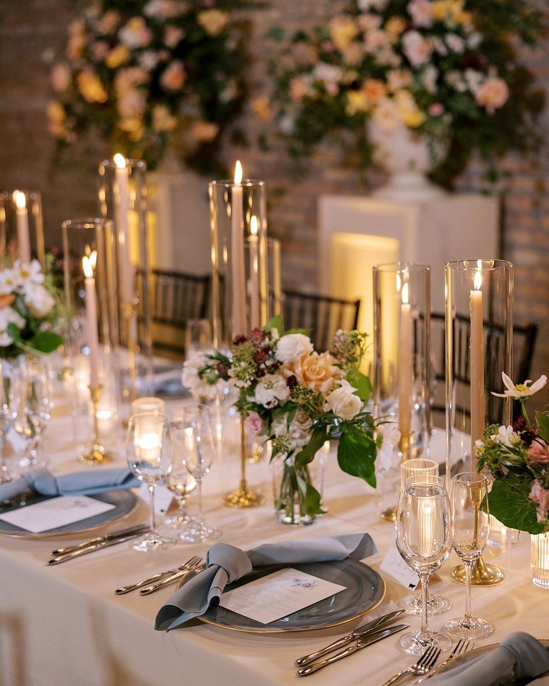 Ivory taper candles in tall glass cylinders on a wedding table with flowers