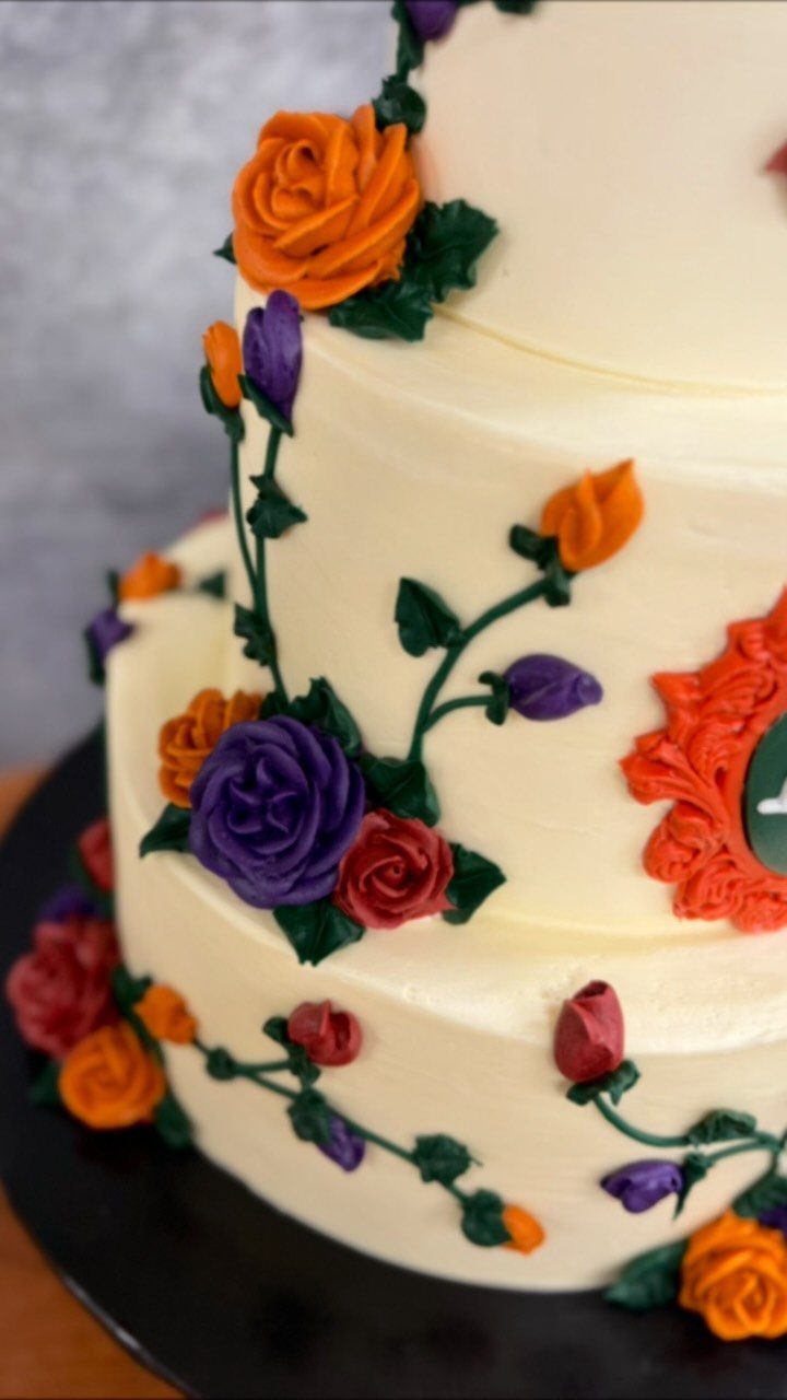 White tiered wedding cake decorated with orange, red, and purple buttercream roses.