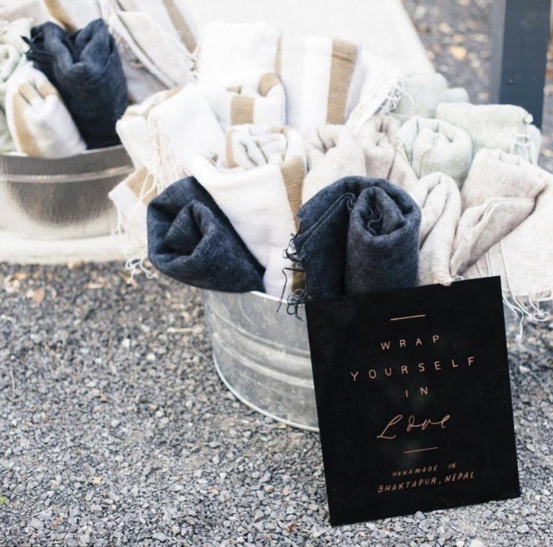 Rolled neutral-toned blankets in metal buckets with a sign saying Wrap Yourself in Love